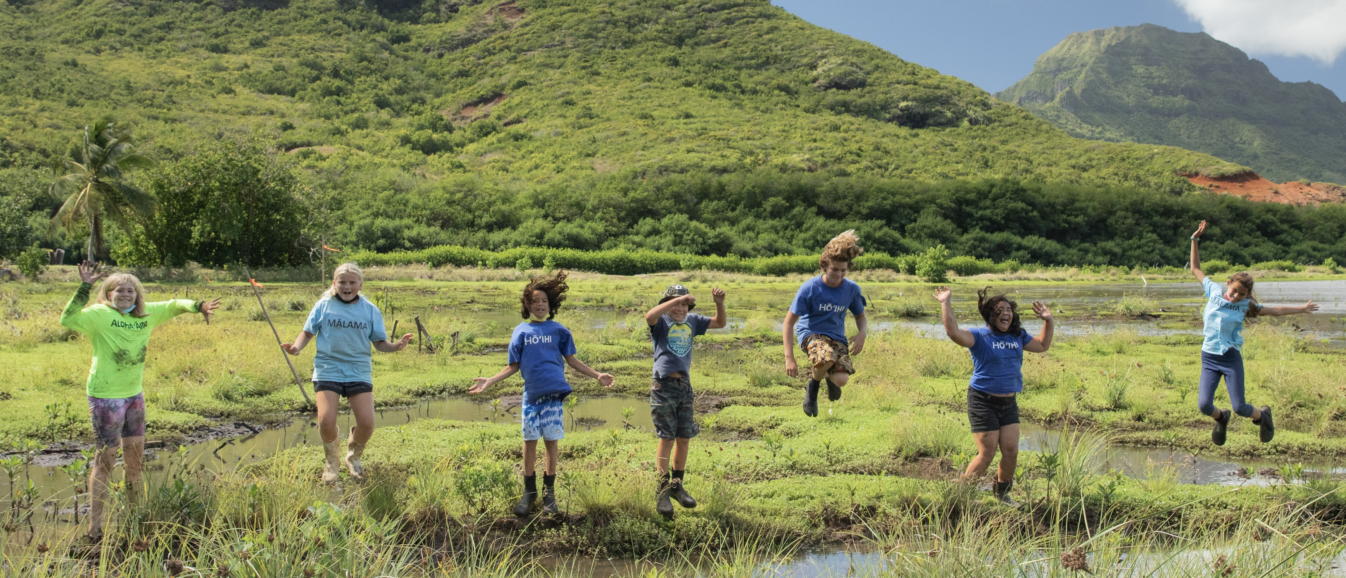 Children jumping in the wetlands with green mountains behind them